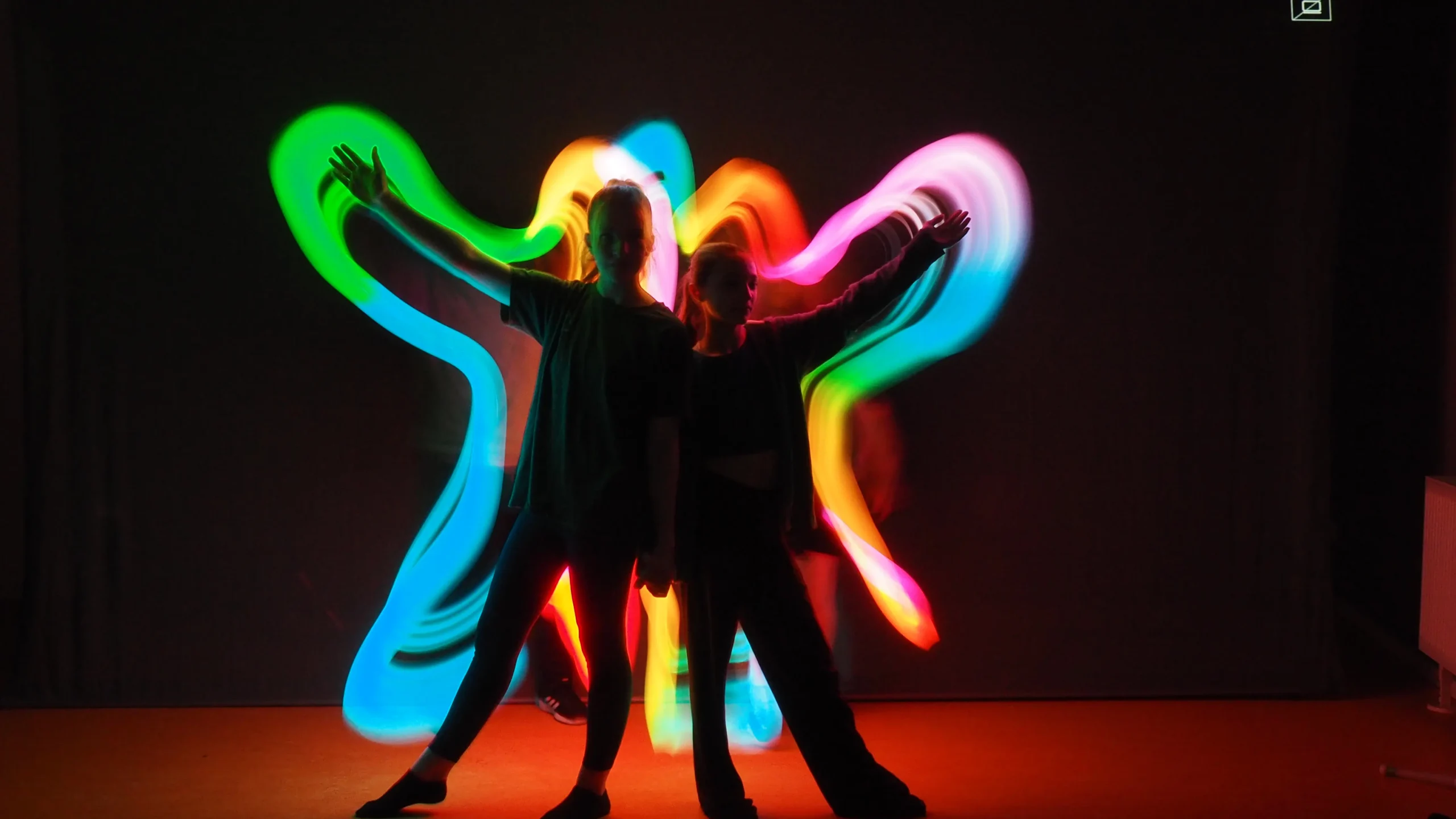 Zwei Personen in dunkler Umgebung von bunten Lichtstreifen umgeben