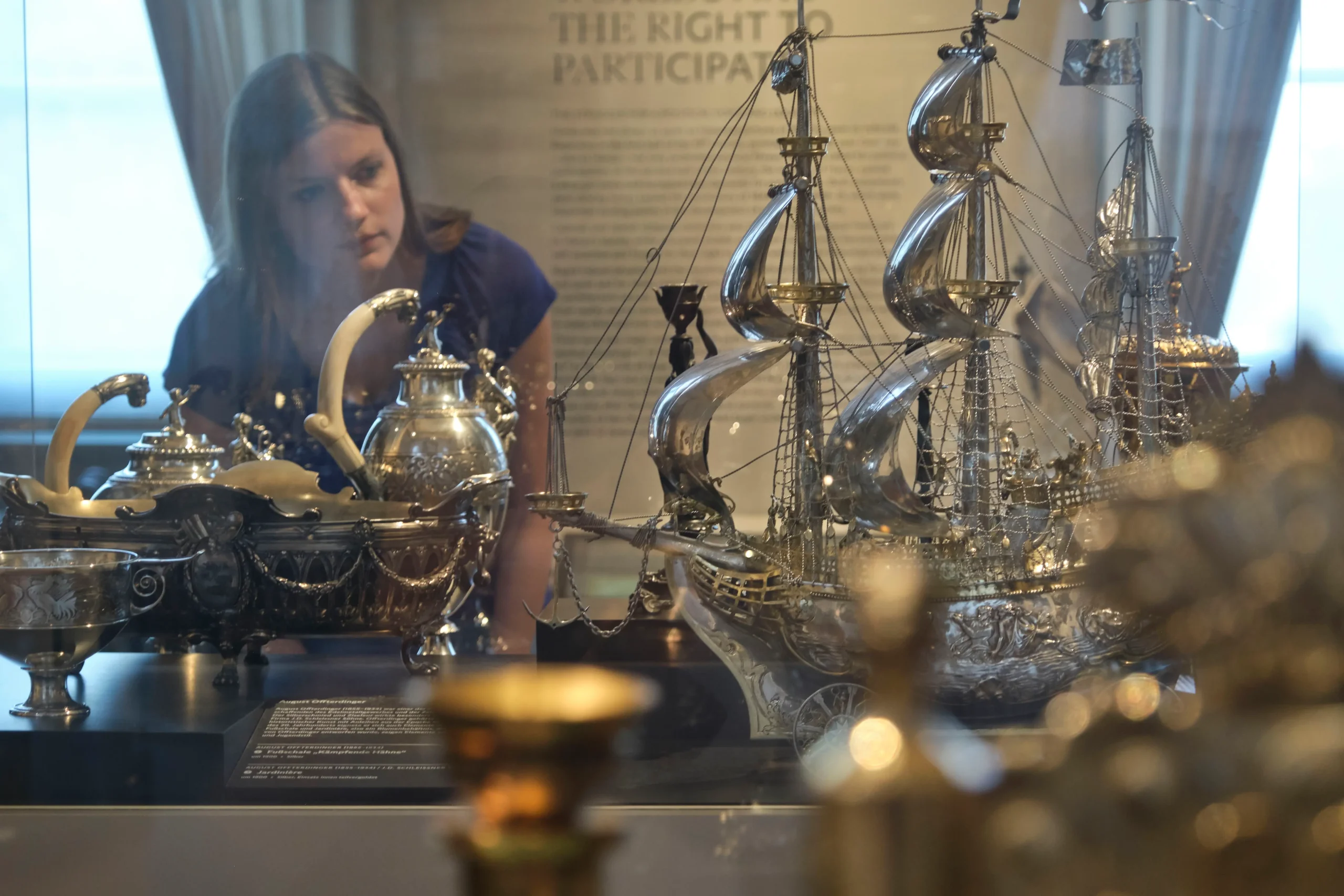 Bild von einer Frau im Museum Phillipsruhe, die sich einen Schiff aus Metall in einer Vitrine anguckt