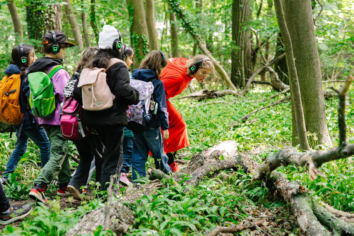 Eine Performerin schleicht mit einer Gruppe von jungen Menschen durch den Wald