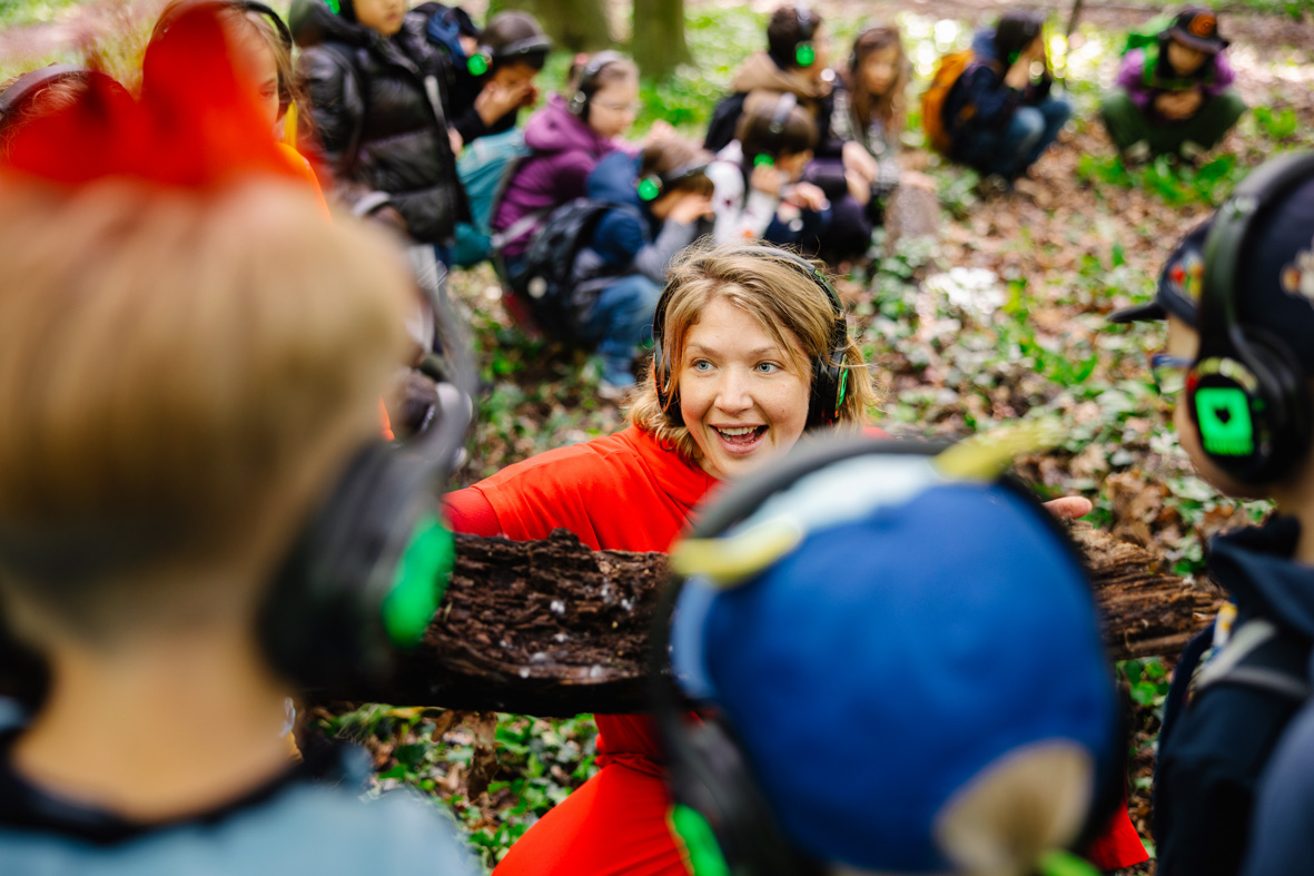 Performerin erklärt Gruppe von jungen Menschen etwas im Wald